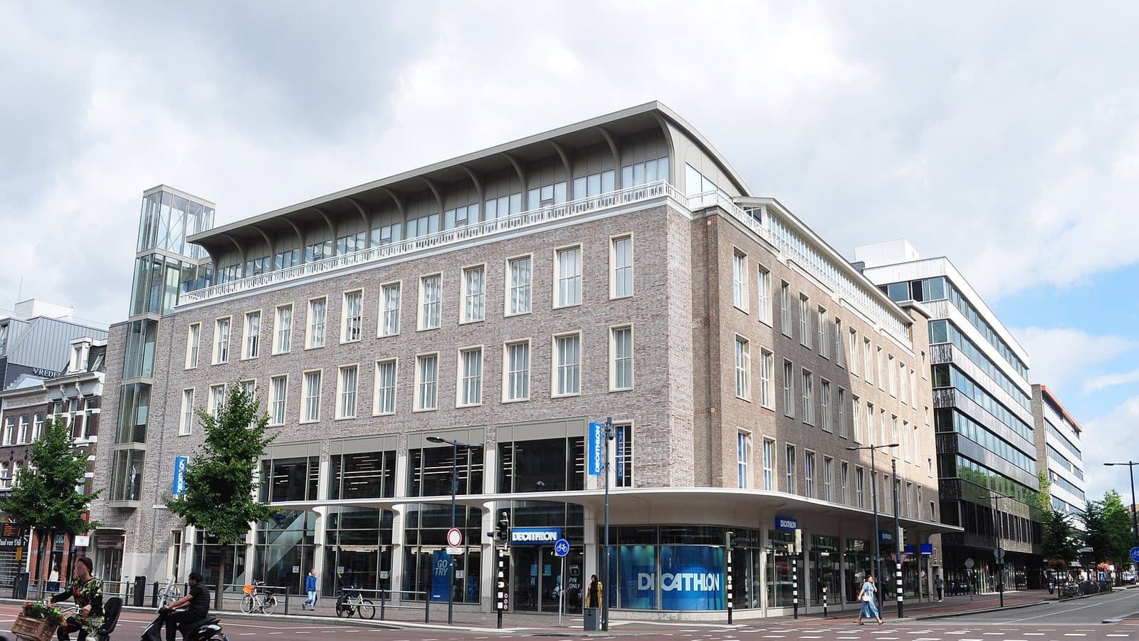Decathlon-winkel aan het Vredenburg in Utrecht met fietsers en een scooter op de kruising ervoor; archieffoto uit 2020