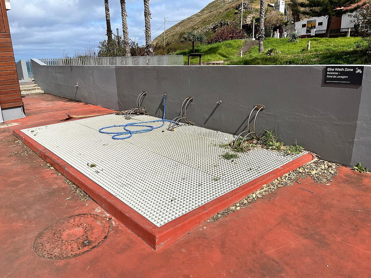 Fietswasplaats met drie fietsbeugels, een blauwe waterslang en een bord met de tekst Bike Wash Zone naast een grijze muur