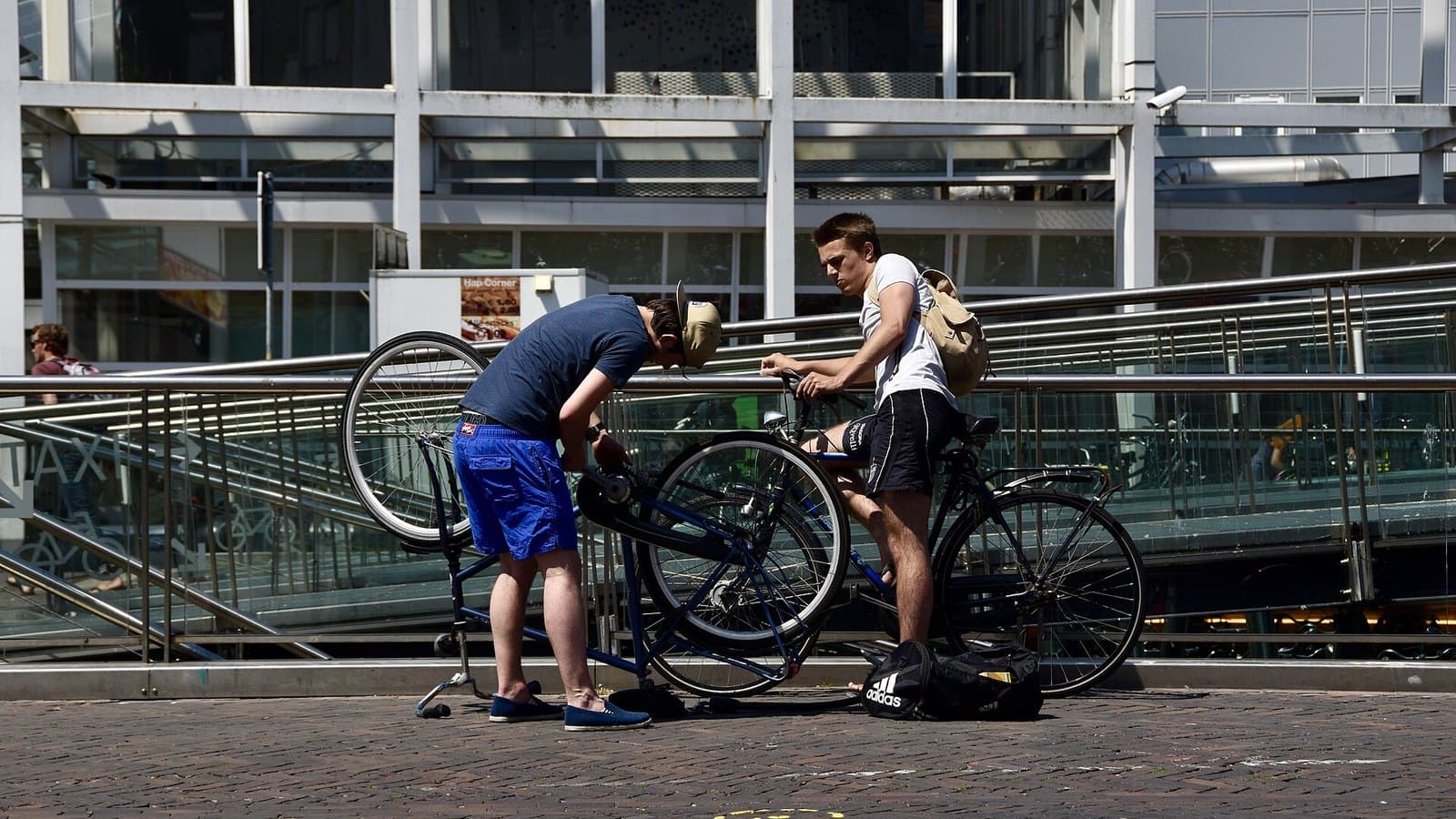 Twee jonge mannen sleutelen aan een omgekeerde stadsfiets bij de fietsenstalling van station Leiden Centraal; archieffoto uit 2015, niet van EasyFiets