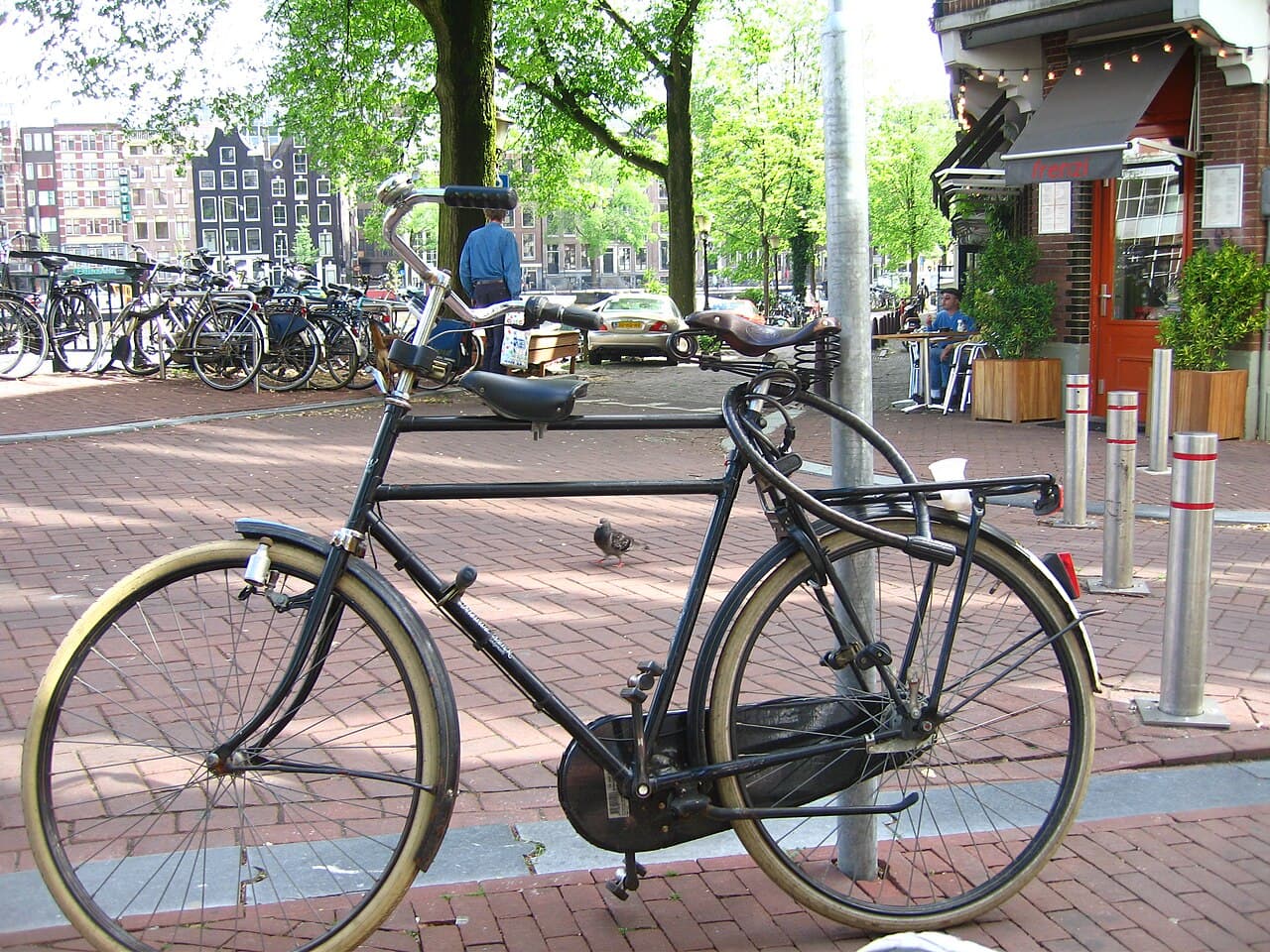 Zwarte stadsfiets met een beugelslot vastgezet aan een lantaarnpaal op een Amsterdamse straat