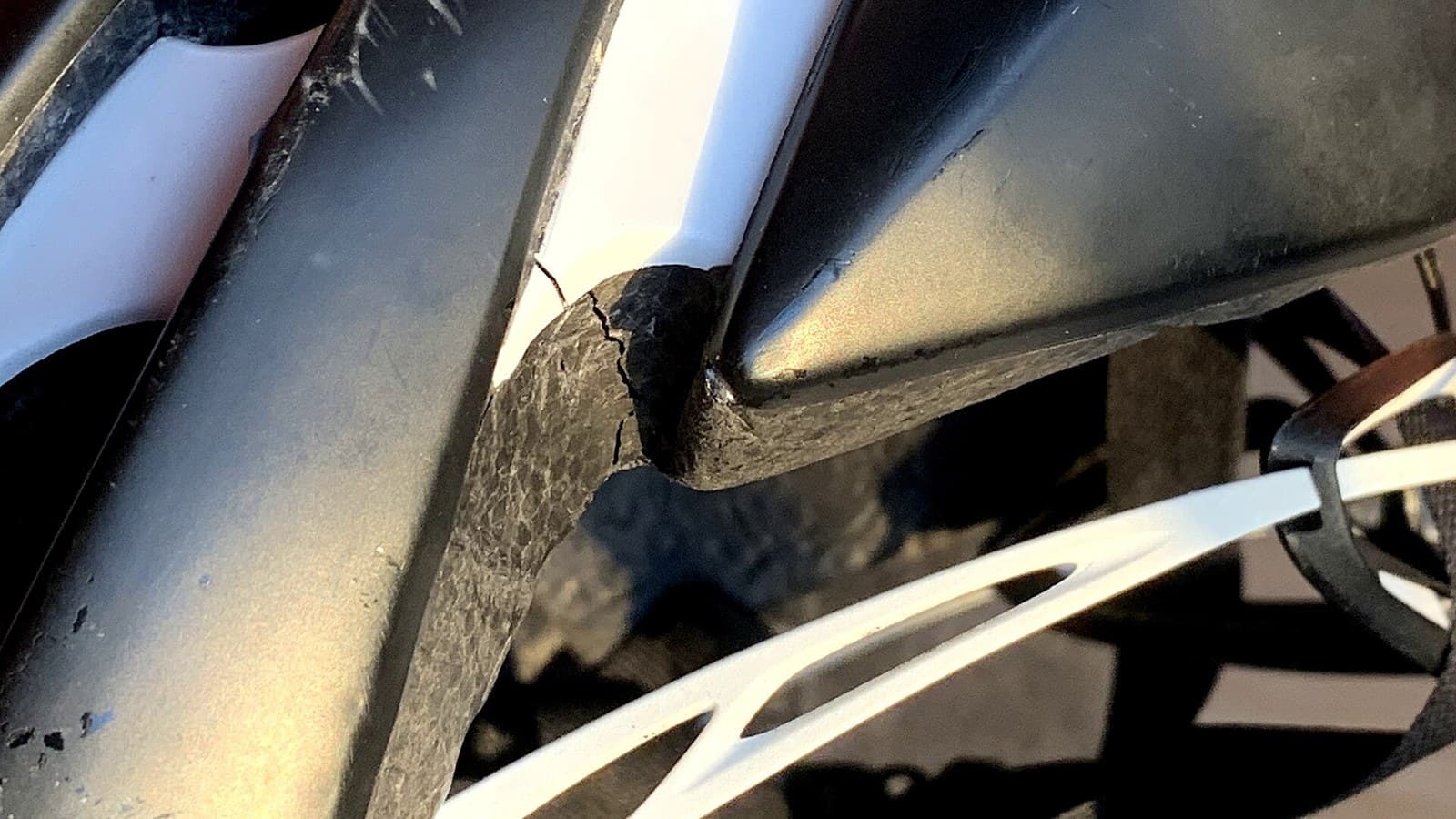 Close-up van een zwart-witte fietshelm met een scheur dwars door de buitenschaal en het schuim, ontstaan bij een val