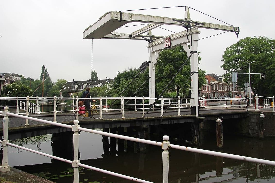 Fietser op een gele fiets met roze fietstas rijdt over de witte ophaalbrug Zijlpoortsbrug in Leiden, gezien vanaf de kade met witte leuningen