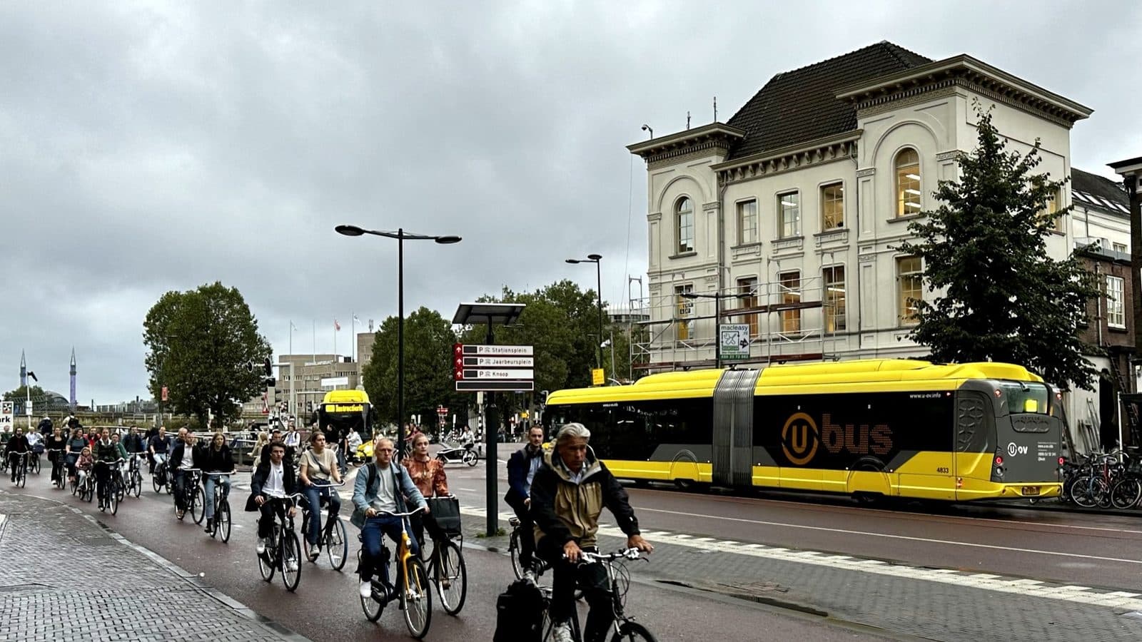 Groep forenzen op fietsen in de ochtendspits op het Vredenburg in Utrecht, met een gele stadsbus ernaast