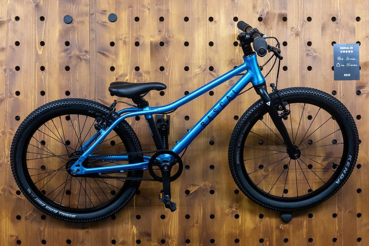 Blauwe Rascal 20 kinderfiets met 20 inch wielen en zwarte noppenbanden, hangend aan een houten wand op de Eurobike-beurs van 2024
