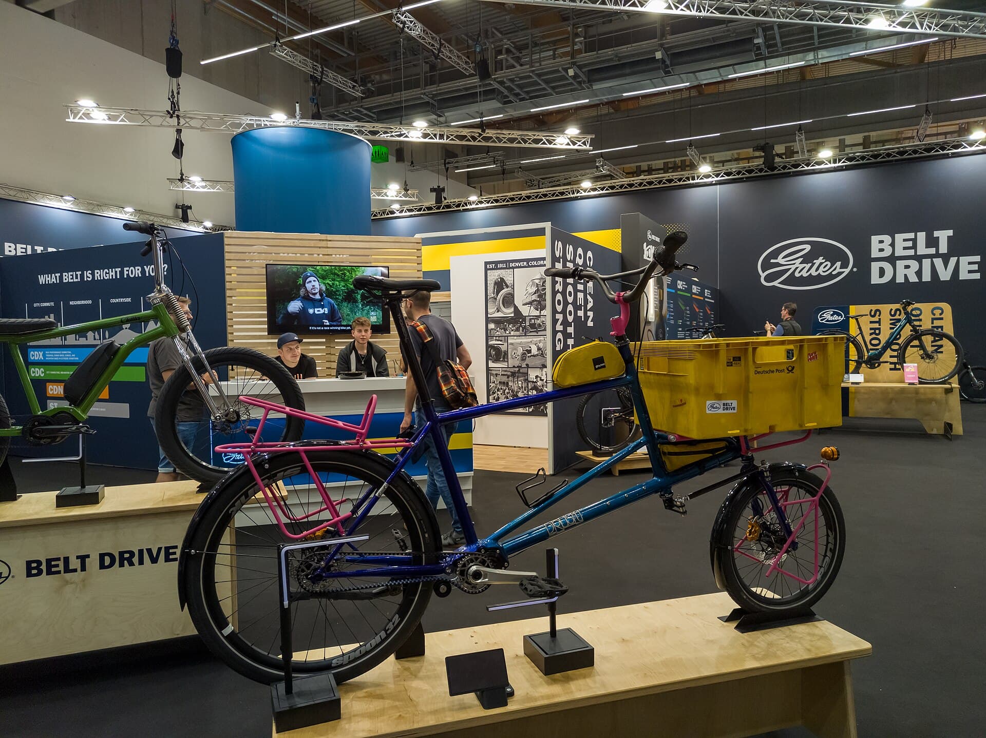 Blauwe transportfiets met roze dragers, gele kratten en een Gates-riemaandrijving op de stand van Gates tijdens Eurobike 2024 in Frankfurt