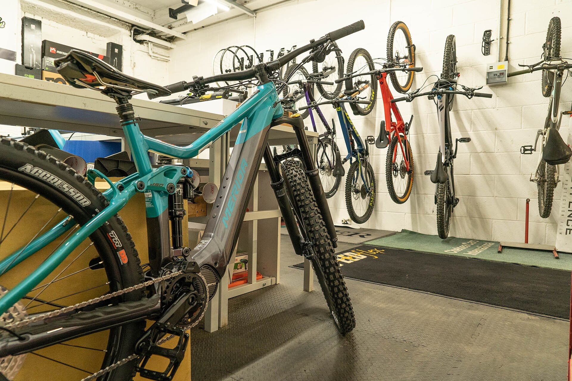 Elektrische mountainbike met middenmotor in een fietswerkplaats, met aan de muur erachter een rij opgehangen fietsen
