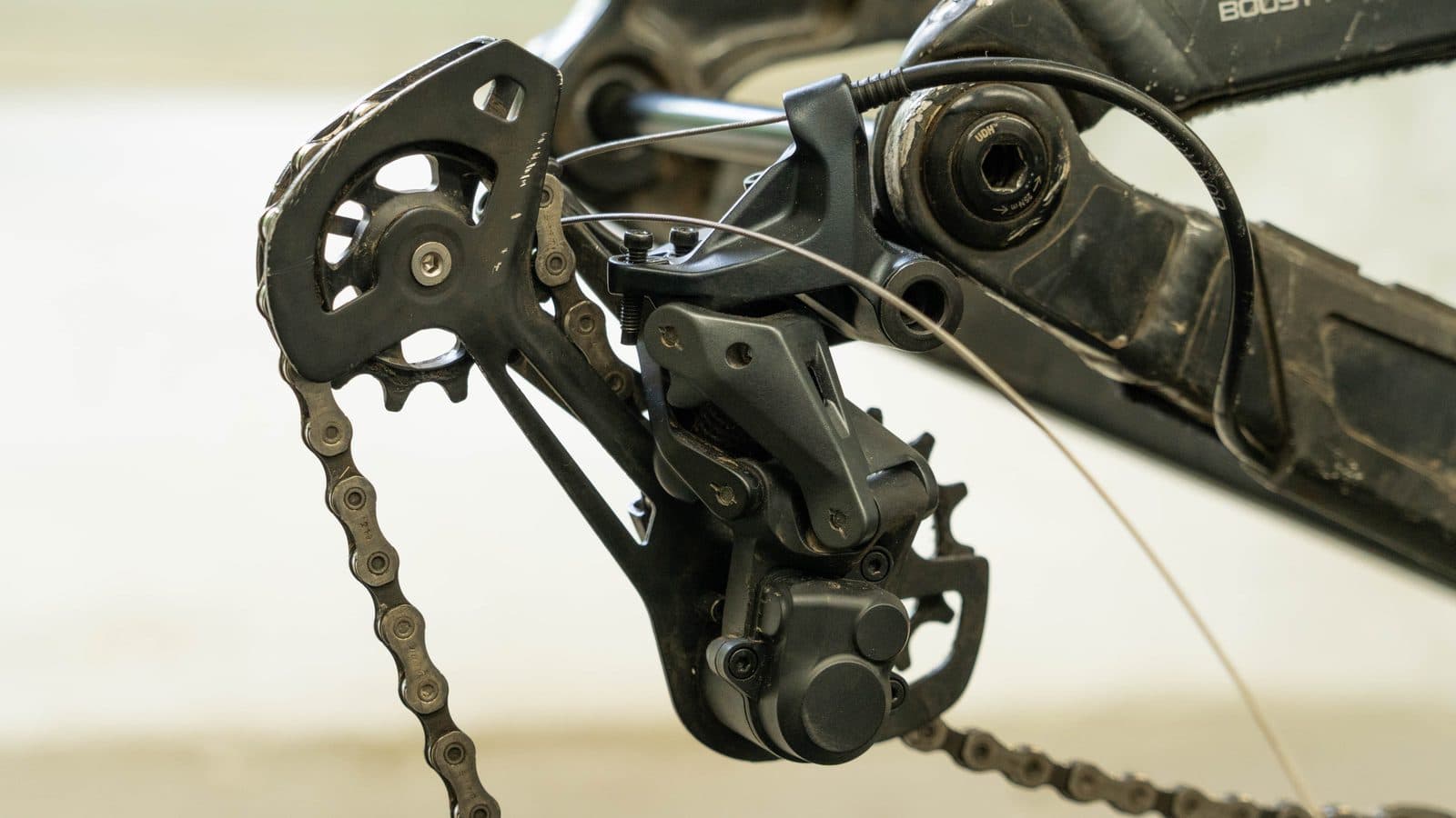 Close-up van een zwarte achterderailleur met ketting, versnellingskabel en geleidewieltjes onder het frame van een fiets