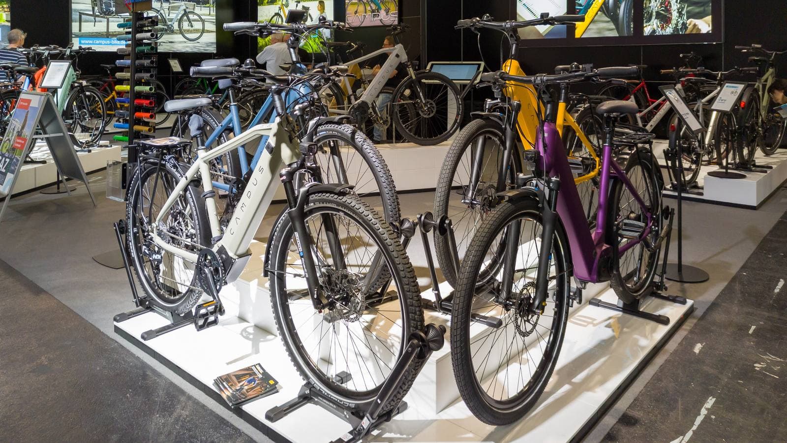Rij nieuwe elektrische fietsen met accu in het frame, opgesteld op een beursstand met informatiebordjes ernaast