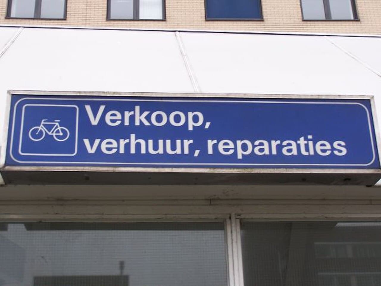 Blauw uithangbord met een fietsicoon en de tekst Verkoop, verhuur, reparaties boven een fietsenwinkel bij station Amersfoort