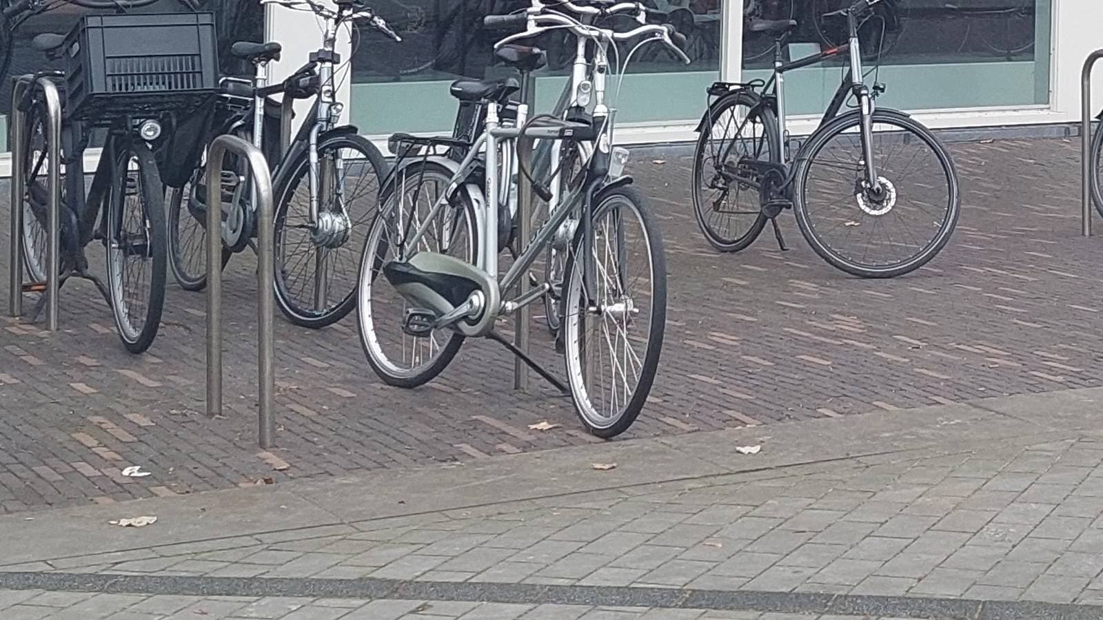 Rij Nederlandse stadsfietsen naast elkaar geparkeerd in een fietsenrek op een bestrating voor een fietsenwinkel