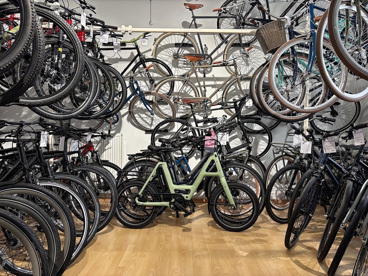 Volle fietsenwinkel van binnen, met fietsen aan wandhaken en een lichtgroene compacte e-bike in het midden; archieffoto uit een winkel in München, niet van Velo Cyclo